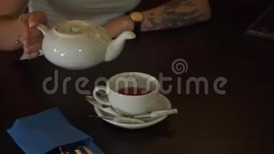 茶被倒入玻璃透明茶杯中。 一杯茶。 糖果，热茶和茶壶.. 陶瓷茶壶和玻璃茶杯特写..
